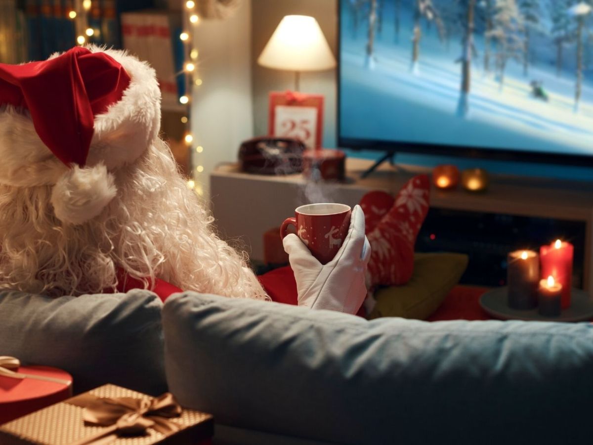 Weihnachtsmann sitzt auf dem Sofa vor dem Fernseher.