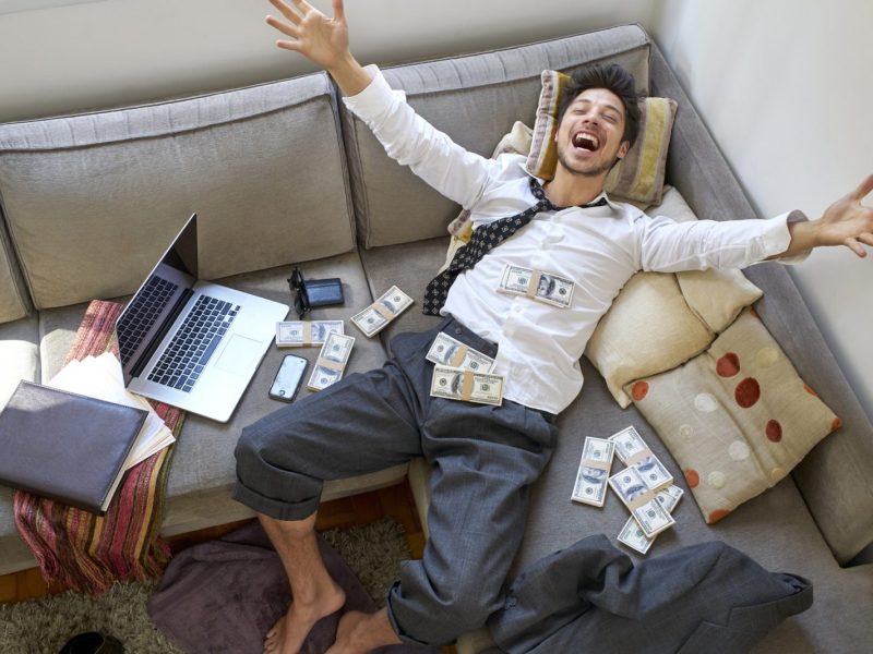 Mann liegt im Geld auf dem Sofa