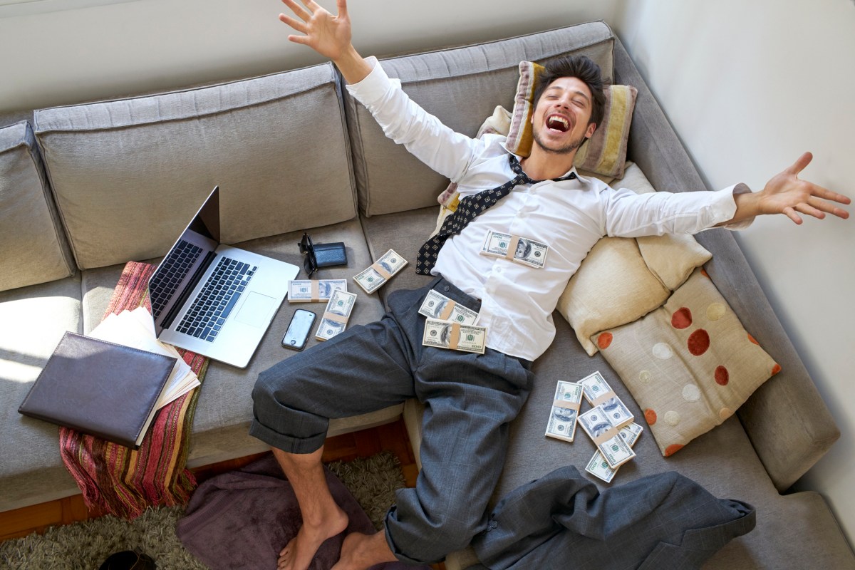 Mann liegt im Geld auf dem Sofa