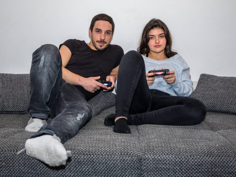 Mann und Frau mit PlayStation Controllern in der Hand auf Sofa