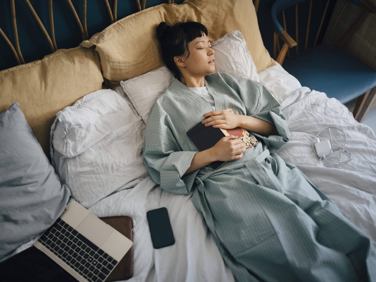 Frau liegt mit Smartphone und Laptop im Bett