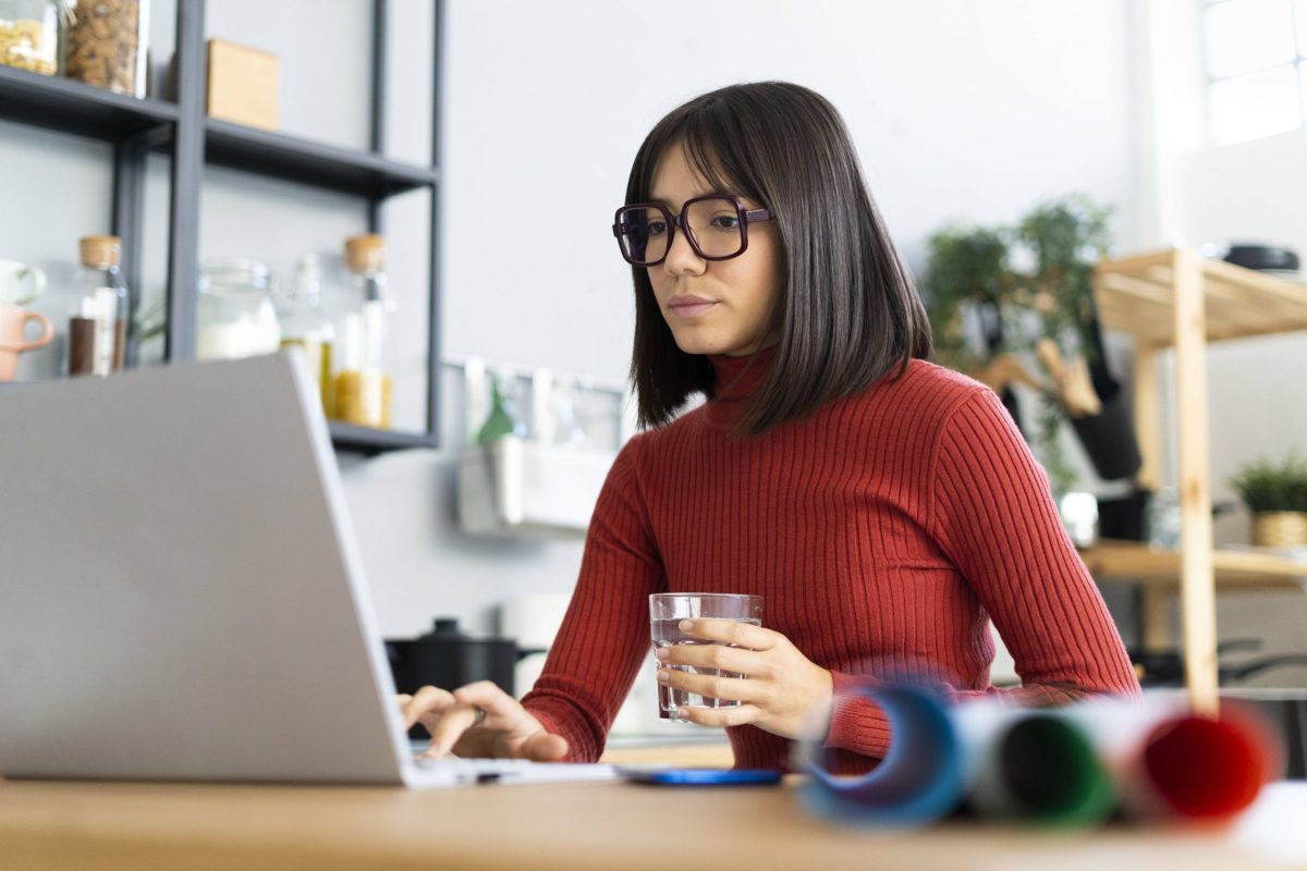 Frau sitzt mit Tasse vor Laptop