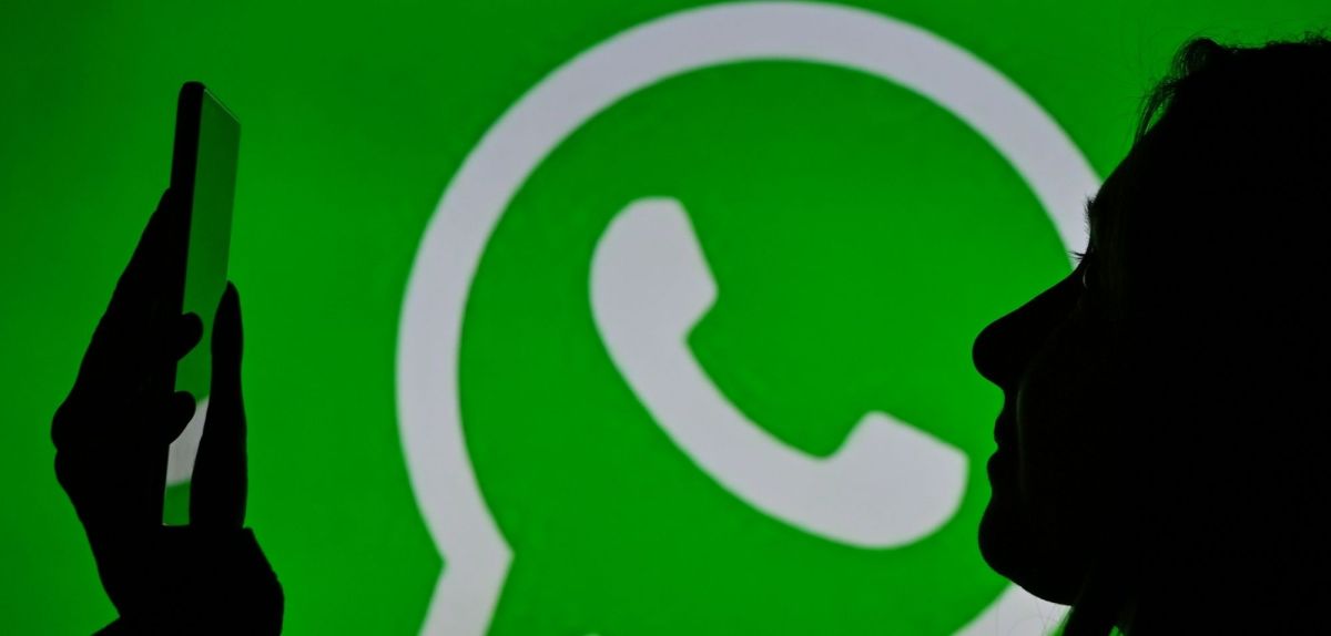 Frau mit Smartphone vor einem WhatsApp-Logo