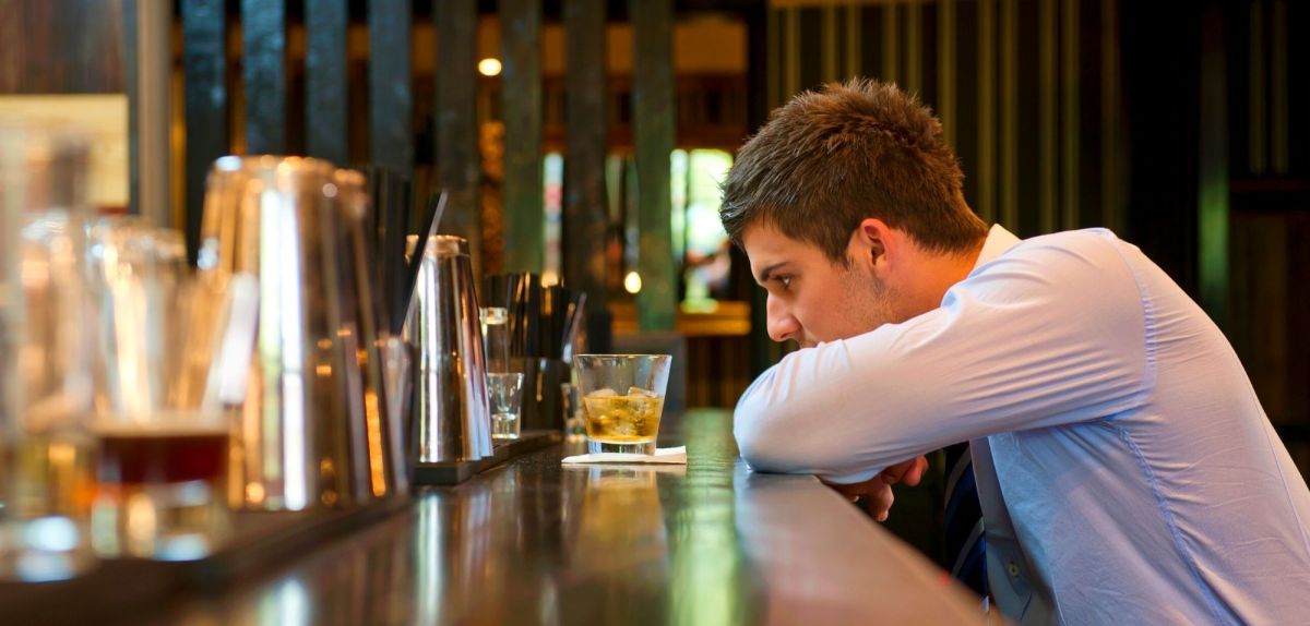 Mann sitzt alleine in einer Bar vor einem alkoholischen Getränk.