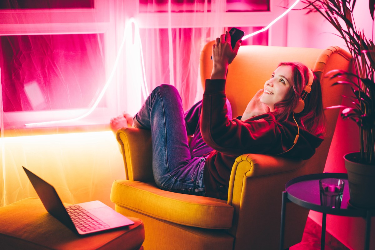 Frau sitzt mit Handy bei rosa Beleuchtung auf einem Sessel