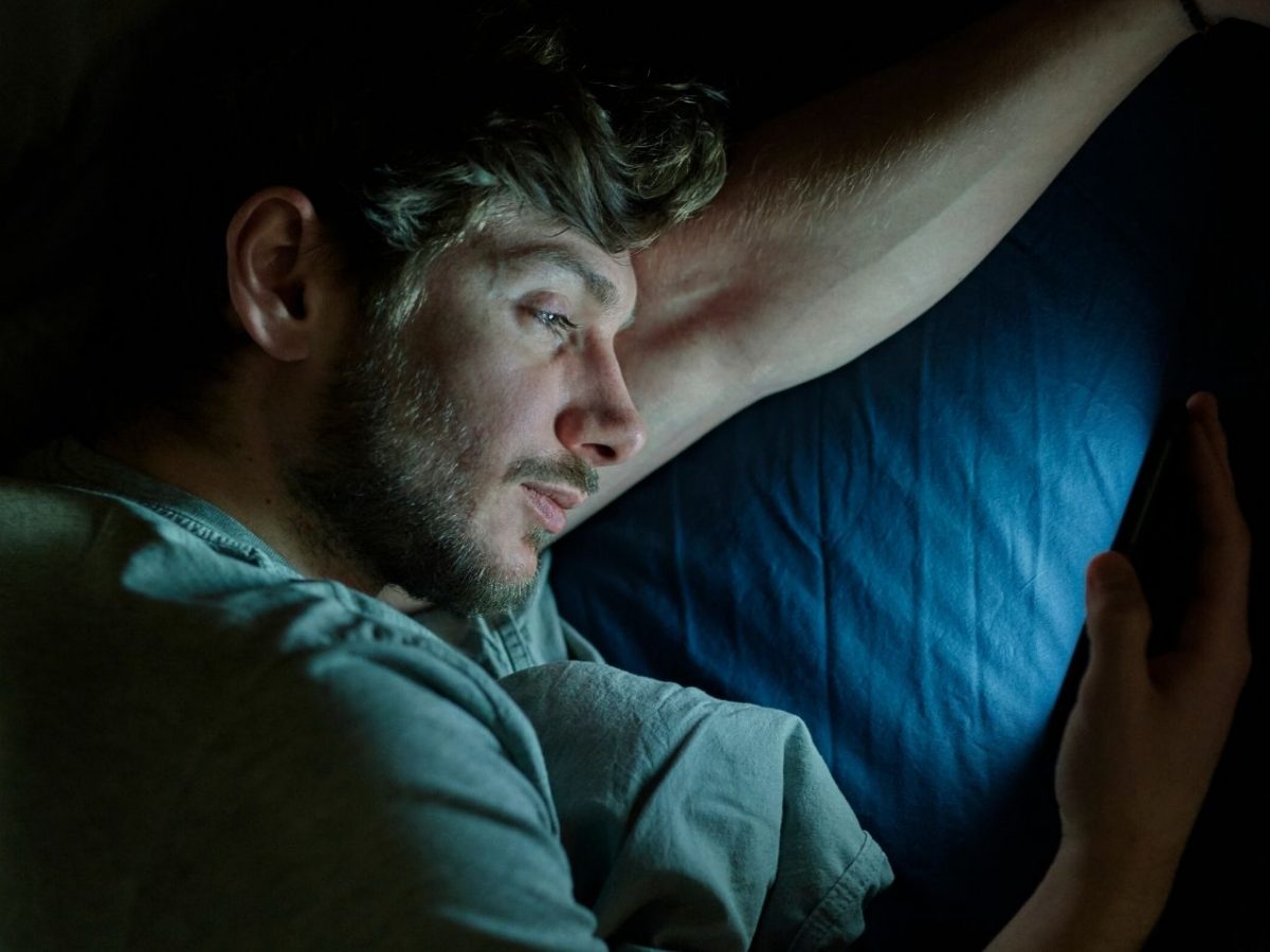 Mann im Dunkeln mit dem Handy im Bett.