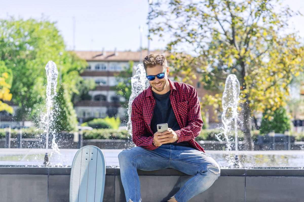 Mann sitzt im Park mit dem Handy in der Hand.