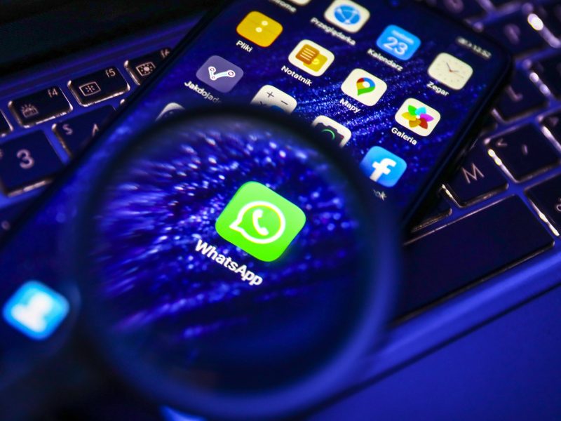 WhatsApp-Logo auf dem Handy wird mit Lupe beleuchtet