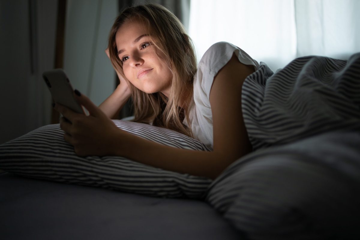 Frau liegt auf Bett und schaut auf ihr Smartphone