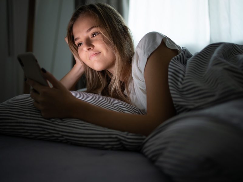 Frau liegt auf Bett und schaut auf ihr Smartphone