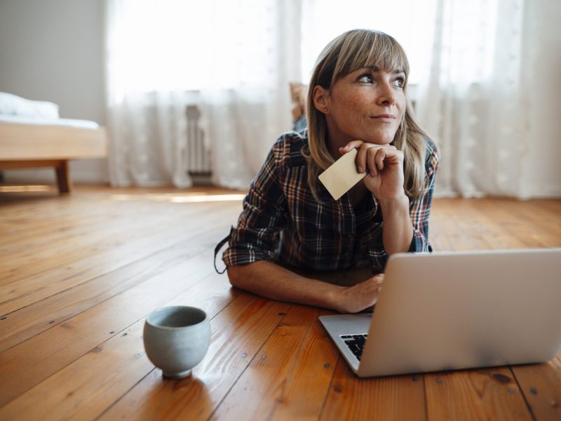 Frau liegt vor Laptop mit Bankkarte in der Hand