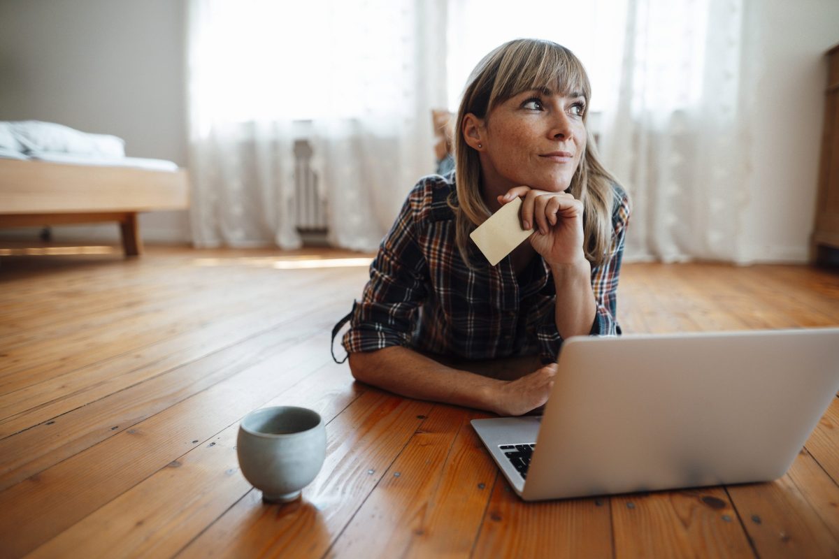 Frau liegt vor Laptop mit Bankkarte in der Hand