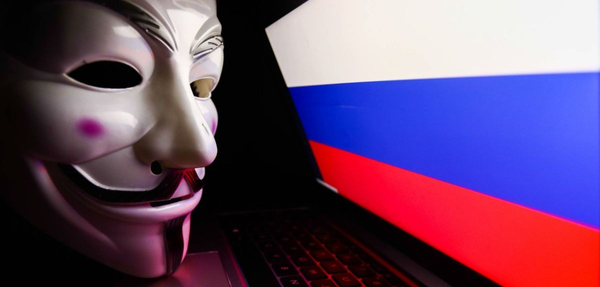 Anonymous-Maske vor einem Laptop. mit Russland-Fahne.