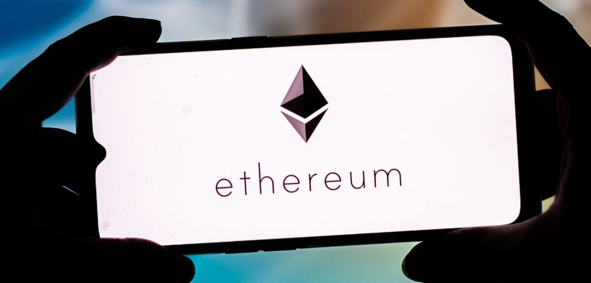 Hände halten Smartphone mit Ethereum-Logo auf dem Display
