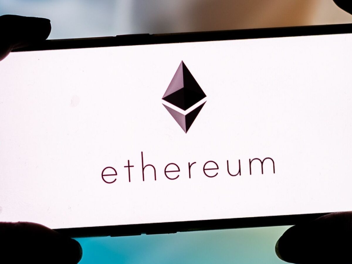 Hände halten Smartphone mit Ethereum-Logo auf dem Display
