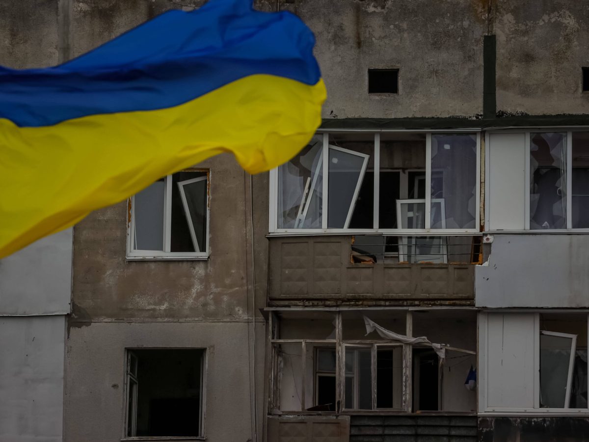 Ukrainische Flagge weht vor verwüstetem Gebäude