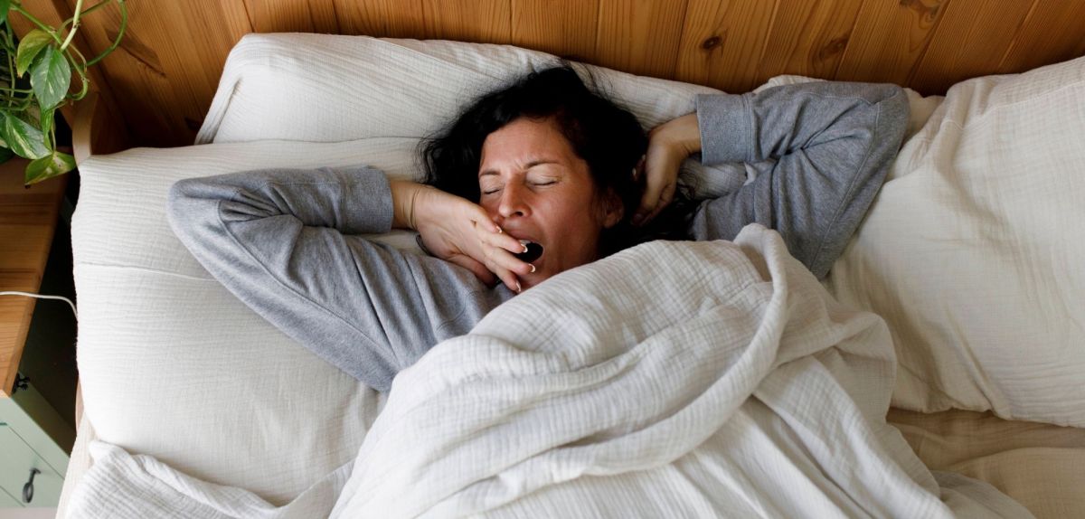 Frau liegt im Bett und gähnt.