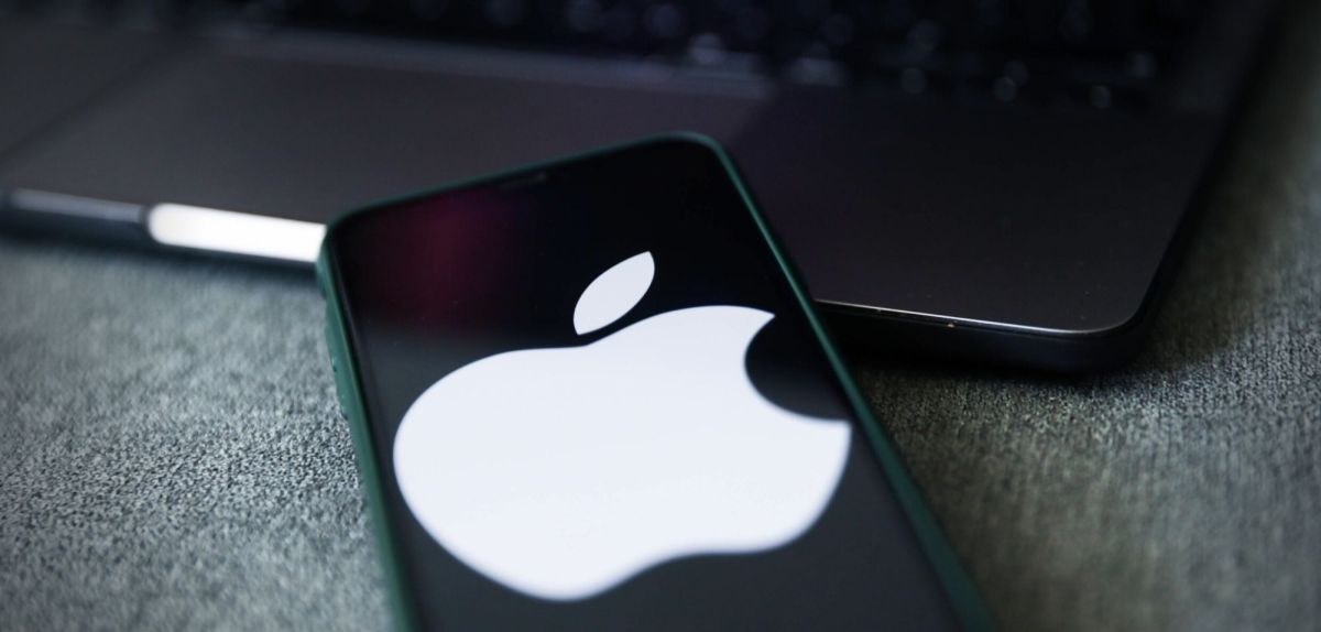 Ein iPhone mit Apple-Logo liegt vor einem Laptop.