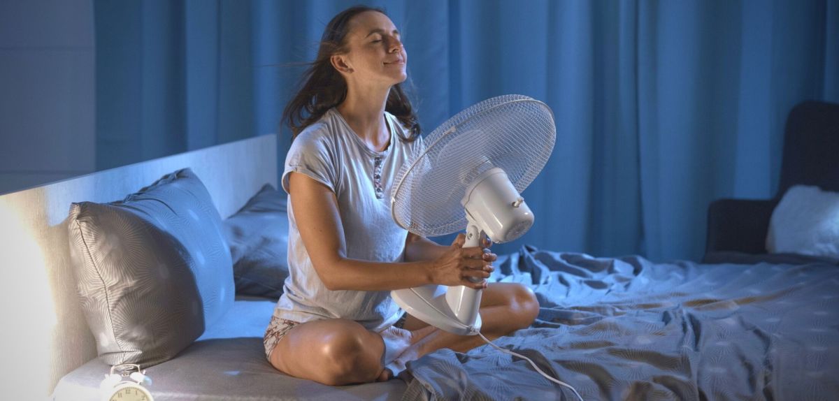 Frau hält sich im Bett Ventilator vor das Gesicht