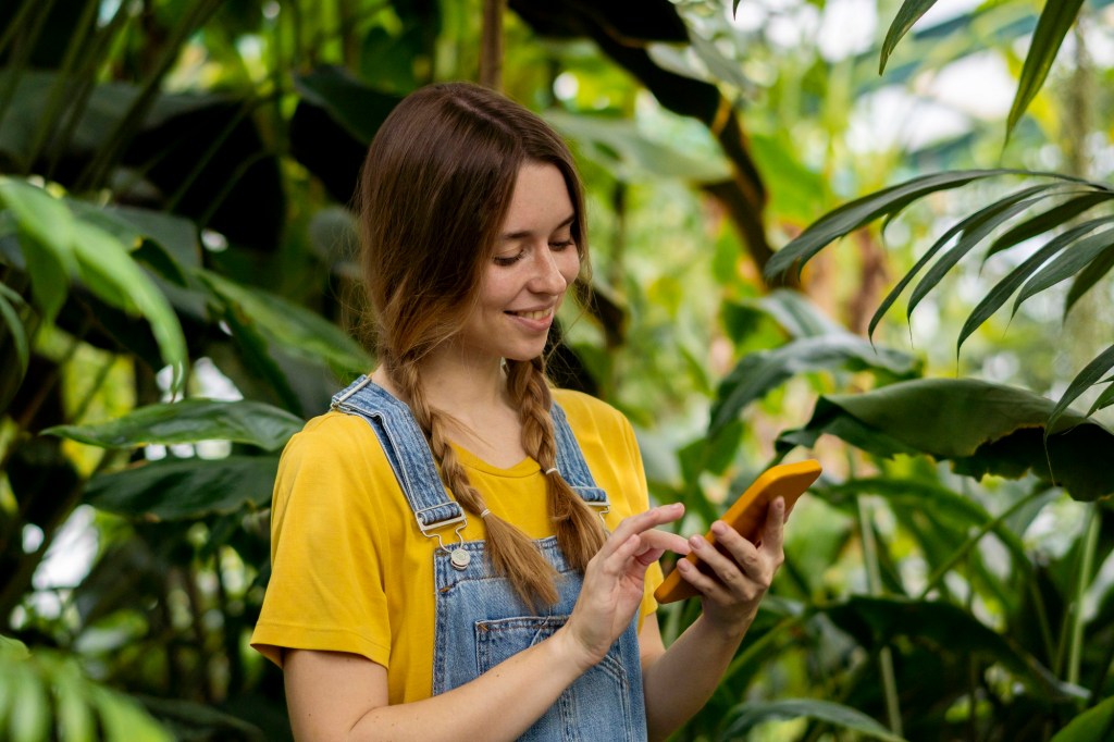 Frau mit Handy vor Grünpflanzen