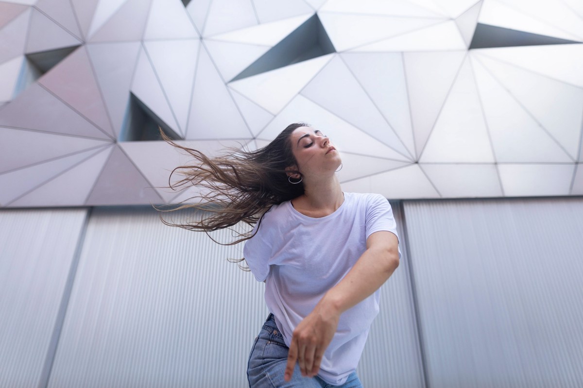 Frau tanzt vor einer futuristisch anmutenden, weißen Fassade