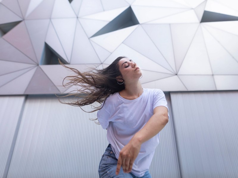 Frau tanzt vor einer futuristisch anmutenden, weißen Fassade