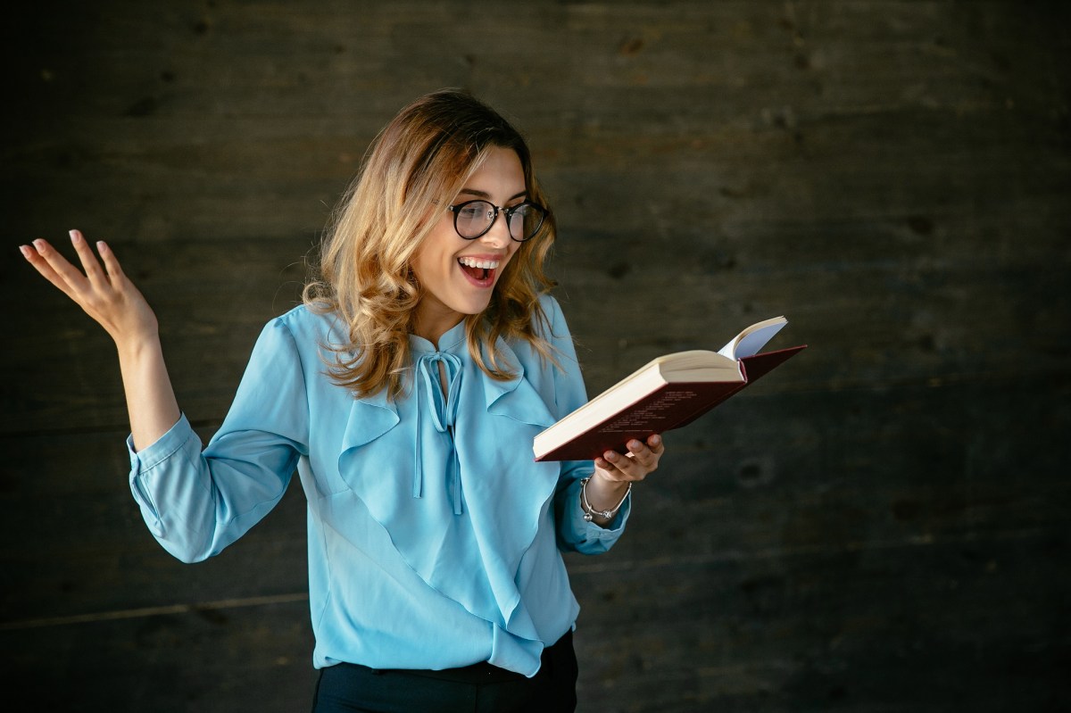 Frau gestikuliert mit einem Buch in der Hand und lacht