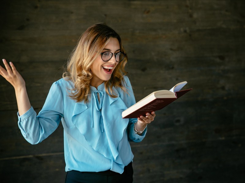 Frau gestikuliert mit einem Buch in der Hand und lacht
