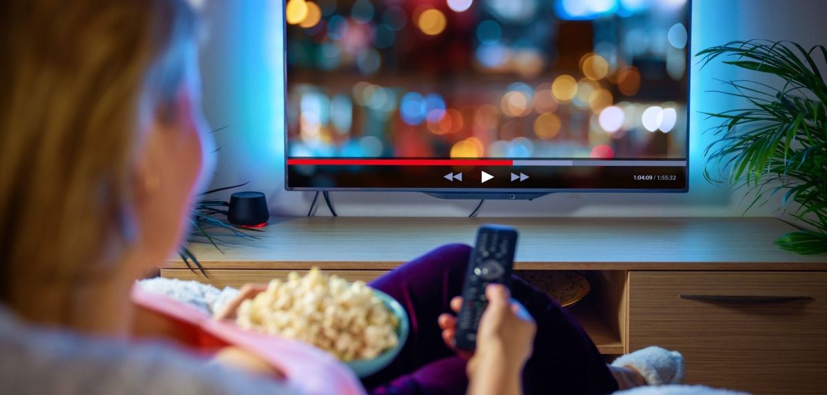 Frau sitzt vor dem Fernseher mit einer Schüssel Popcorn und streamt.