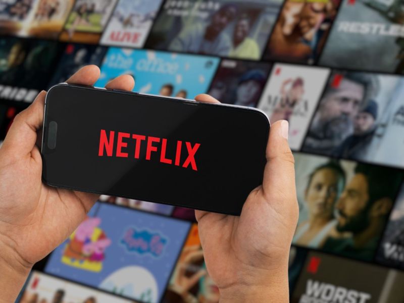 Netflix-Logo auf einem Handy-Display, im Hintergrund viele Kacheln von Filmen und Serien.