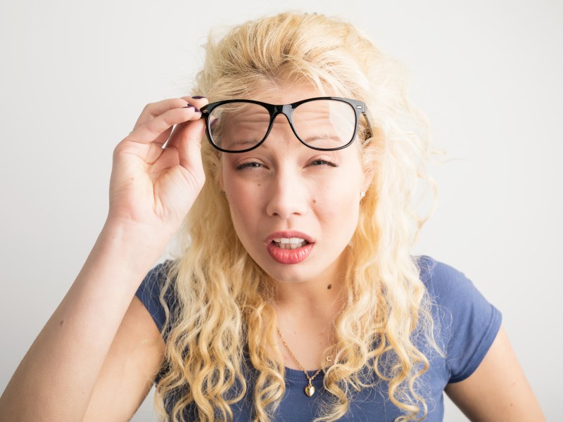 Frau hebt Brille und kneift die Augen zusammen