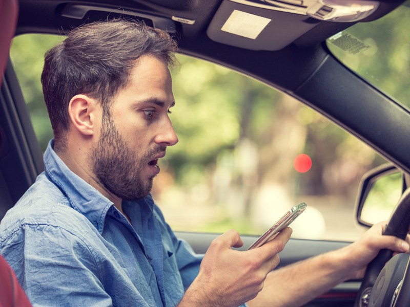 Mann sitzt erstaunt mit Handy im Auto