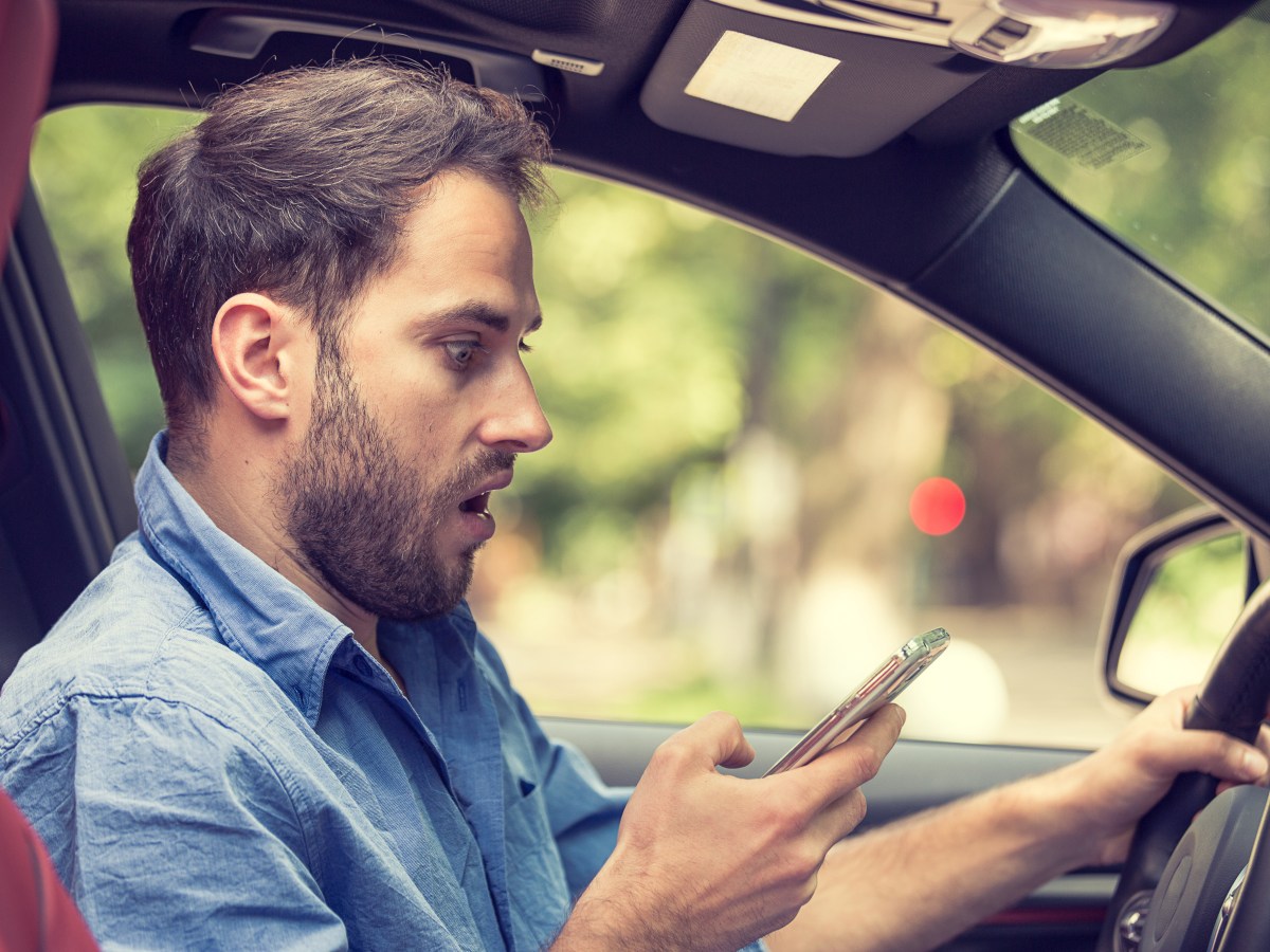 Mann sitzt erstaunt mit Handy im Auto