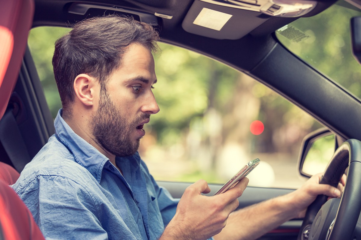 Mann sitzt erstaunt mit Handy im Auto