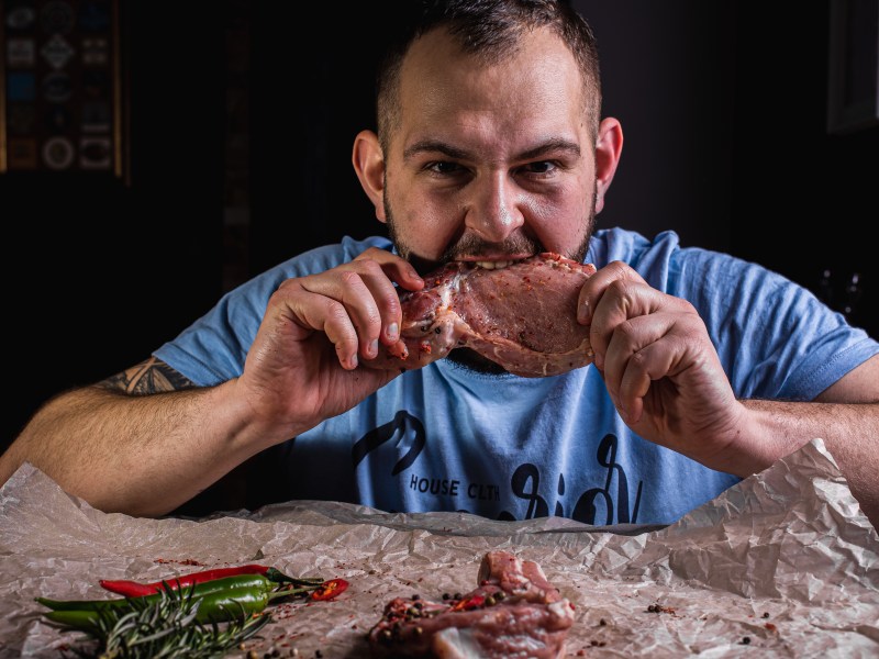 Mann beißt in rohes Fleisch