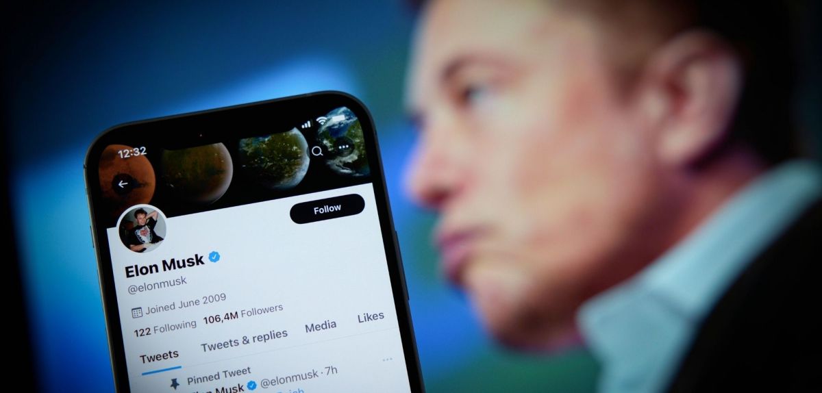 Bild von einem Handy mit Elon Musks Twitter-Profil, im HIntergrund Elon Musk.