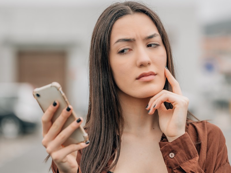 Frau schaut skeptisch auf ihr Smartphone.