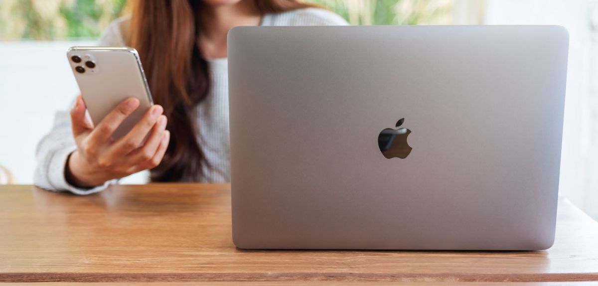 Frau am Tisch mit einem iPhone und einem MacBook.