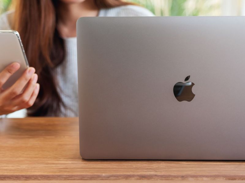 Frau am Tisch mit einem iPhone und einem MacBook.