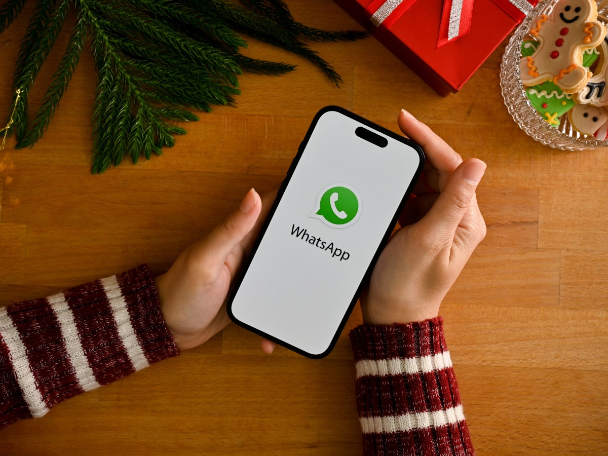 Person hält ein Smartphone mit WhatsApp-Logo über einem weihnachtlich geschmückten Tisch