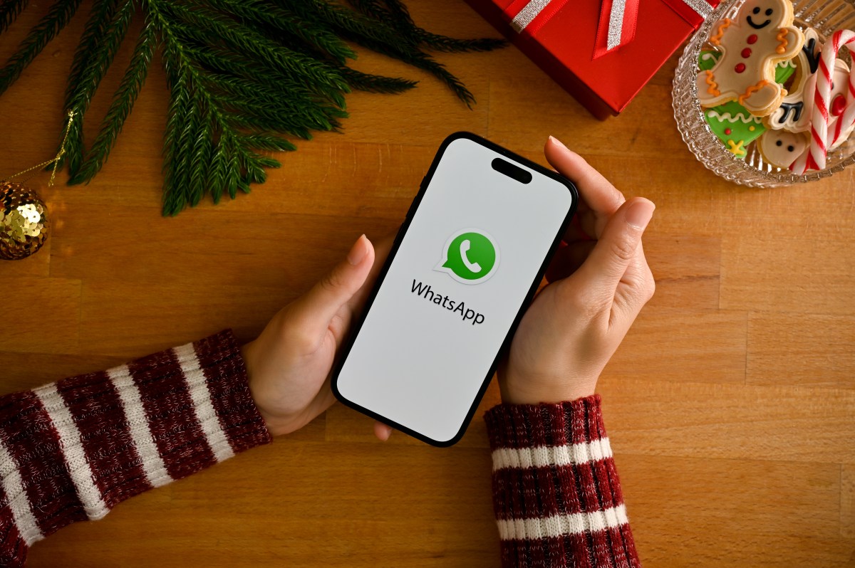 Person hält ein Smartphone mit WhatsApp-Logo über einem weihnachtlich geschmückten Tisch