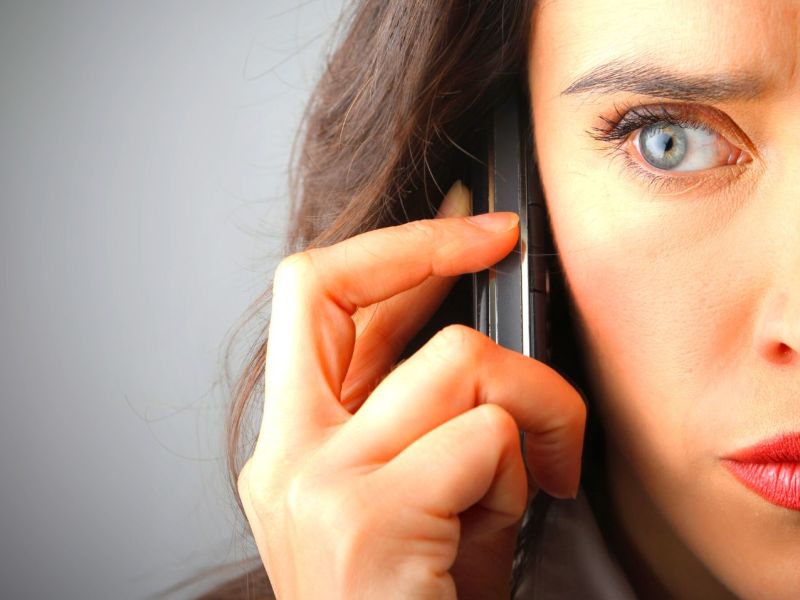 Frau mit skeptischem Blick hält sich Handy ans Ohr.
