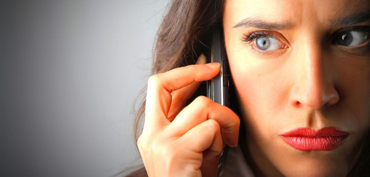 Frau mit skeptischem Blick hält sich Handy ans Ohr.