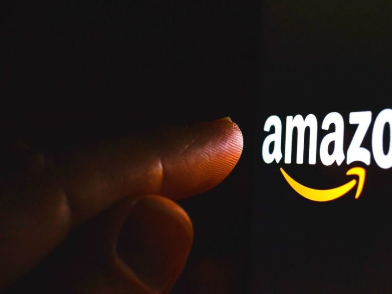 Ein Finger zeigt auf das Amazon-Logo auf einem dunklen Bildschirm.