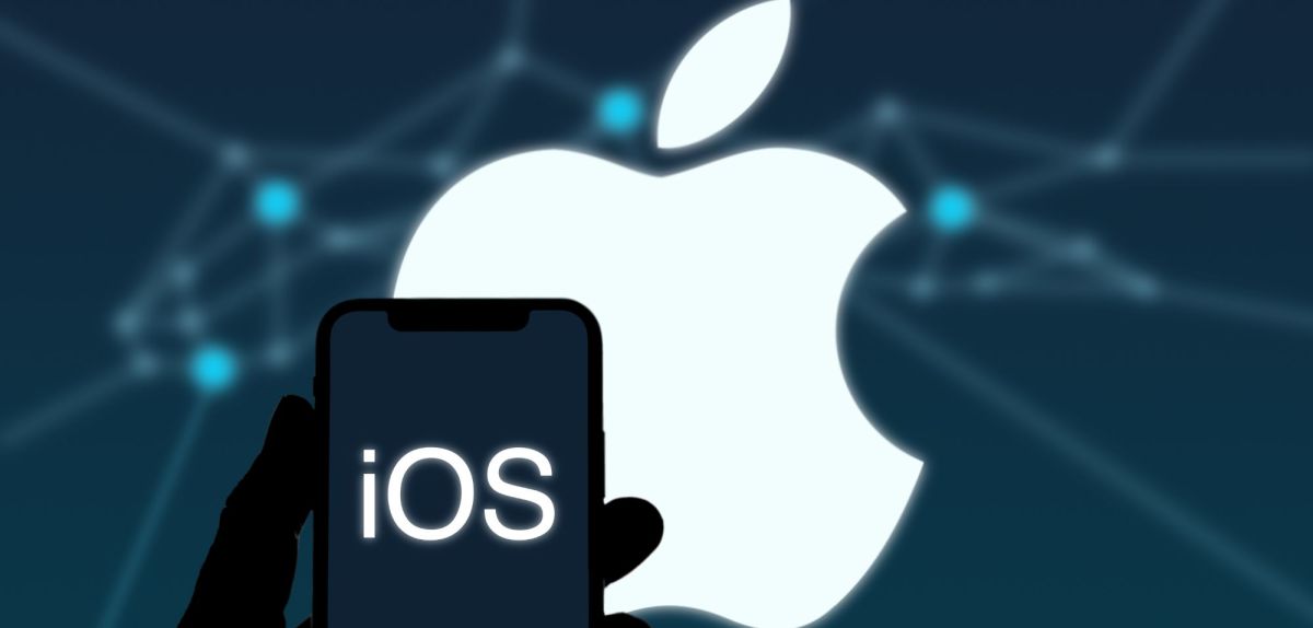 Person hält iPhone mit iOS-Logo in der Hand, Apple-Logo im Hintergrund.