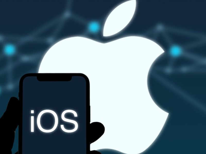 Person hält iPhone mit iOS-Logo in der Hand, Apple-Logo im Hintergrund.