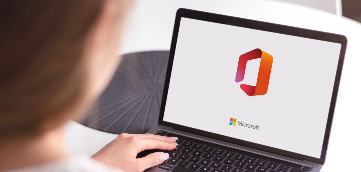Person sitzt vor Laptop, auf dem das Microsoft Office-Logo zu sehen ist.