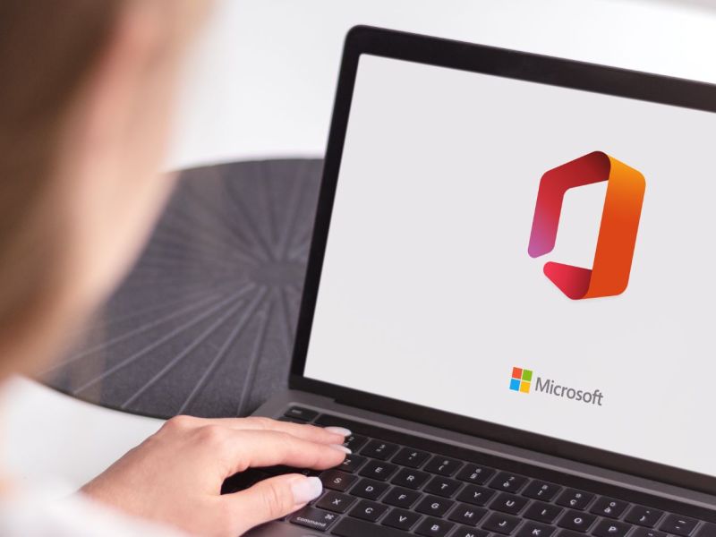Person sitzt vor Laptop, auf dem das Microsoft Office-Logo zu sehen ist.