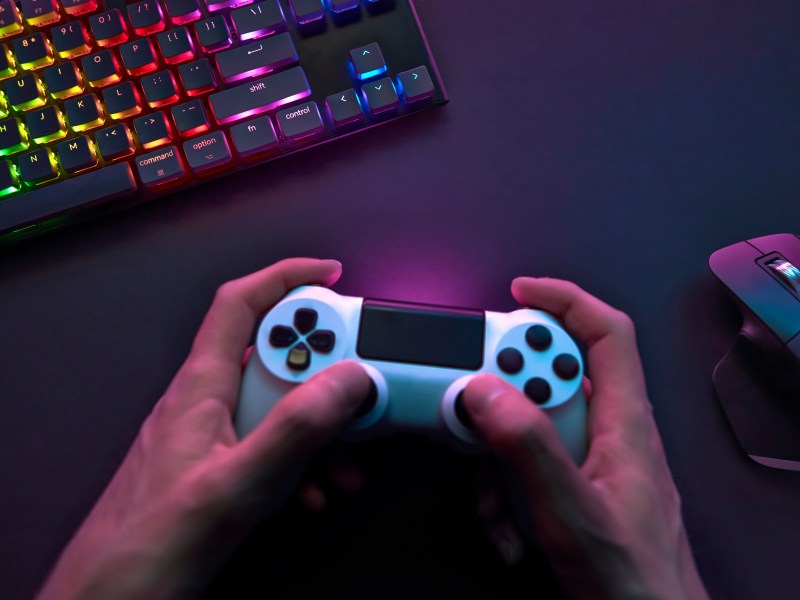 Gaming Controller in Hand vor Maus und Tastatur
