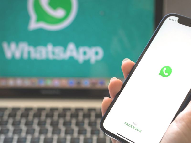WhatsApp-Logo auf einem Handy, im Hintergrund Laptop ebenfalls mit dem Logo.